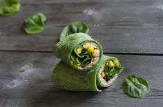 two wraps filled with corn and spinach sitting on top of a wooden table next to leaves