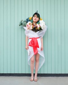 a woman standing in front of a green wall holding flowers