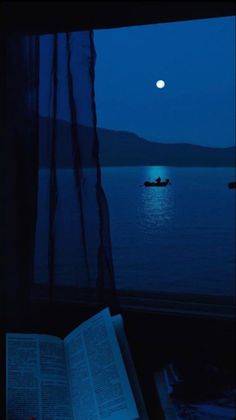 an open book sitting on top of a window sill next to a boat in the water