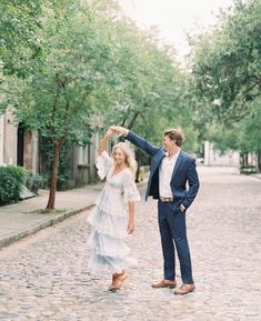 a man and woman dancing in the middle of a cobblestone street with trees lining both sides