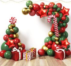 christmas decorations and presents on the floor in front of a white wall with red, green and gold balloons