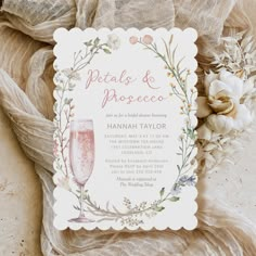 a wedding card with flowers on it and a glass of wine in the middle, next to some burlap fabric