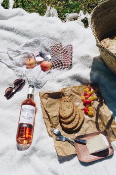 a picnic with bread, fruit and wine on a blanket next to a bottle of wine