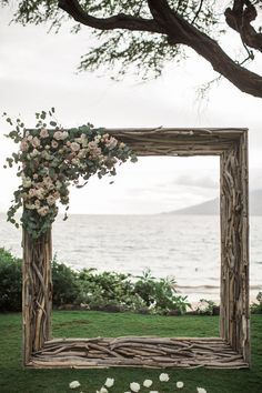 a wooden frame decorated with flowers and greenery on the grass by the water's edge