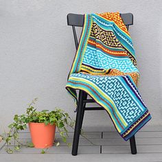 a chair sitting next to a potted plant with a colorful blanket on top of it