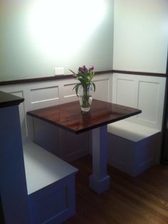 a vase with flowers sitting on top of a wooden table next to two white benches