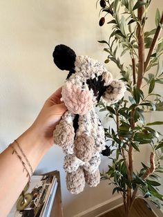 a hand holding a small stuffed animal next to a potted plant