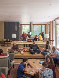 a group of people sitting on couches playing cards in a living room with large windows