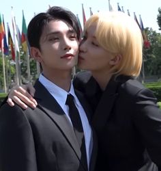 two people in suits and ties kissing each other with flags in the back ground behind them