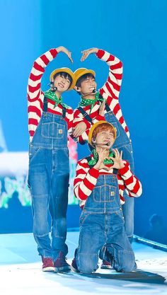 three children in overalls and hats on stage with one child holding his hands up