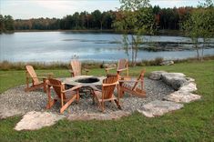 a fire pit surrounded by wooden chairs in front of a lake