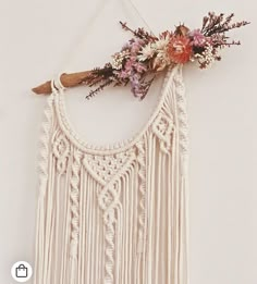 a white wall hanging decorated with flowers and tassels on a wooden stick in front of a white wall