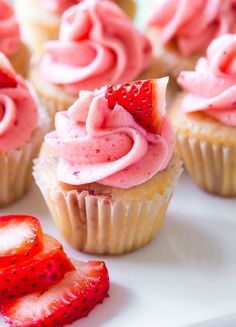 cupcakes with pink frosting and strawberries on a white plate next to some sliced strawberries