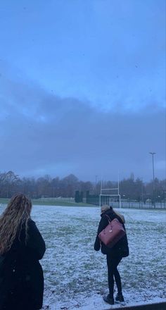 two women are standing in the snow near a soccer field