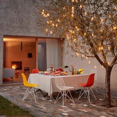 an outdoor dining area with white table and yellow chairs under a tree covered in lights