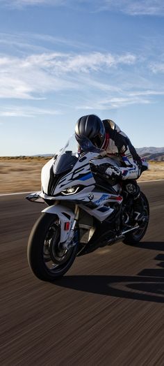 a man riding on the back of a white motorcycle down a street next to a dirt field