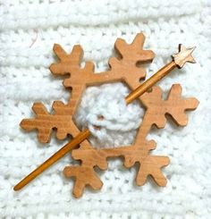 two wooden snowflakes are on a white knitted surface, one is holding a knitting needle