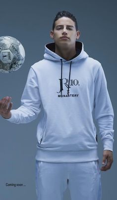 a man is holding a soccer ball in his right hand and wearing a white hoodie