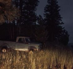 an old pick up truck parked in the middle of a grassy field at night time