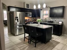 a kitchen with stainless steel appliances and black cabinets, marble counter tops, and white tile flooring