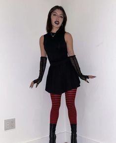 a woman in black dress and red striped stockings posing for the camera with her hands on her hips