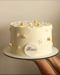 a hand holding a white cake with yellow flowers