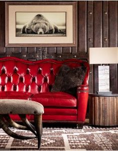 a red leather couch sitting in front of a painting on the wall next to a table