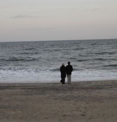 two people standing on the beach looking out at the ocean