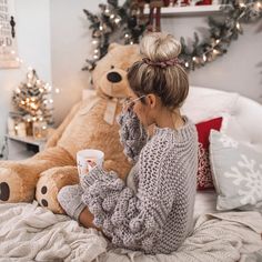 a woman sitting on a bed next to a teddy bear and holding a coffee cup