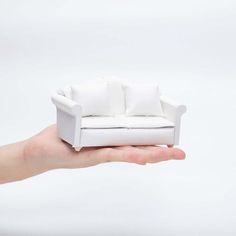 a miniature white couch sitting on top of a person's hand in front of a white background