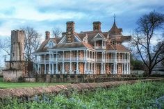 an old house with blue flowers in front of it and trees on the other side