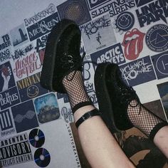 a person wearing black shoes and fishnet stockings standing in front of a wall covered with records