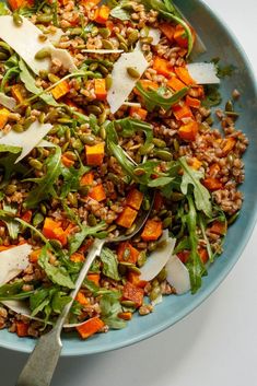 a blue bowl filled with lots of veggies next to a fork and spoon