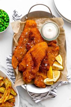 fish and chips on a plate next to peas, lemon wedges, and sour cream