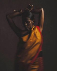 a woman in a yellow and red dress is posing for a photo with her hands on her head