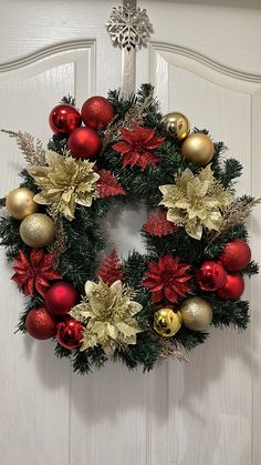 a christmas wreath with poinsettis and other ornaments hanging on a white door