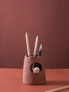 a pen holder with pencils in it on a table next to a red wall