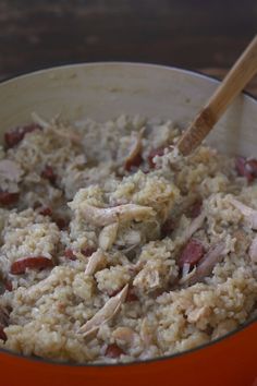 a bowl filled with rice and meat on top of a wooden table next to a spoon