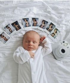 a baby laying on top of a white bed next to polaroid pictures and a camera