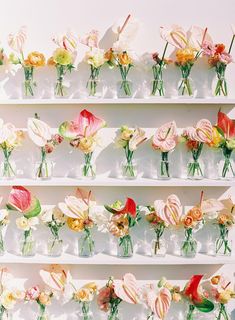 several glass vases filled with flowers sitting on top of a white shelf next to each other