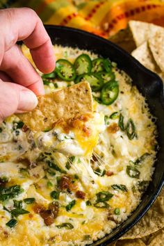 a hand dipping a tortilla chip into a skillet filled with quesadilla