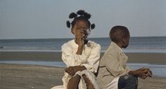 two children sit on the beach and look at something in their hands as they talk to each other