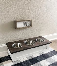 a dog bowl holder with three bowls in it and a love sign on the wall