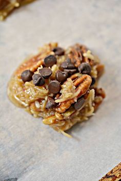 a cookie with chocolate chips and pecans on top sitting on a piece of parchment paper