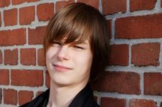 a young man standing next to a brick wall with his eyes closed and looking up