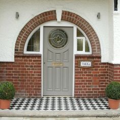 the front entrance to a brick building with potted plants on either side and an arched door