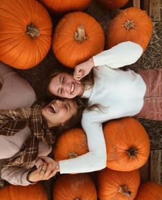 two women standing next to each other surrounded by pumpkins