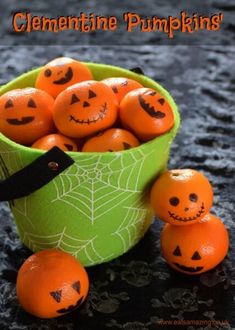 a green bowl filled with oranges sitting on top of a black table next to pumpkins