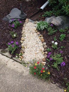 a garden with flowers and rocks in the ground next to a stone path that is bordered by mulch