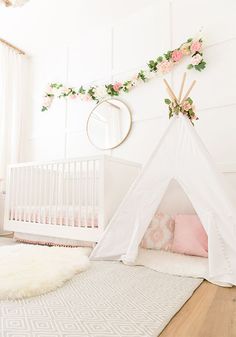 a white teepee with pink flowers and greenery on the wall next to a crib